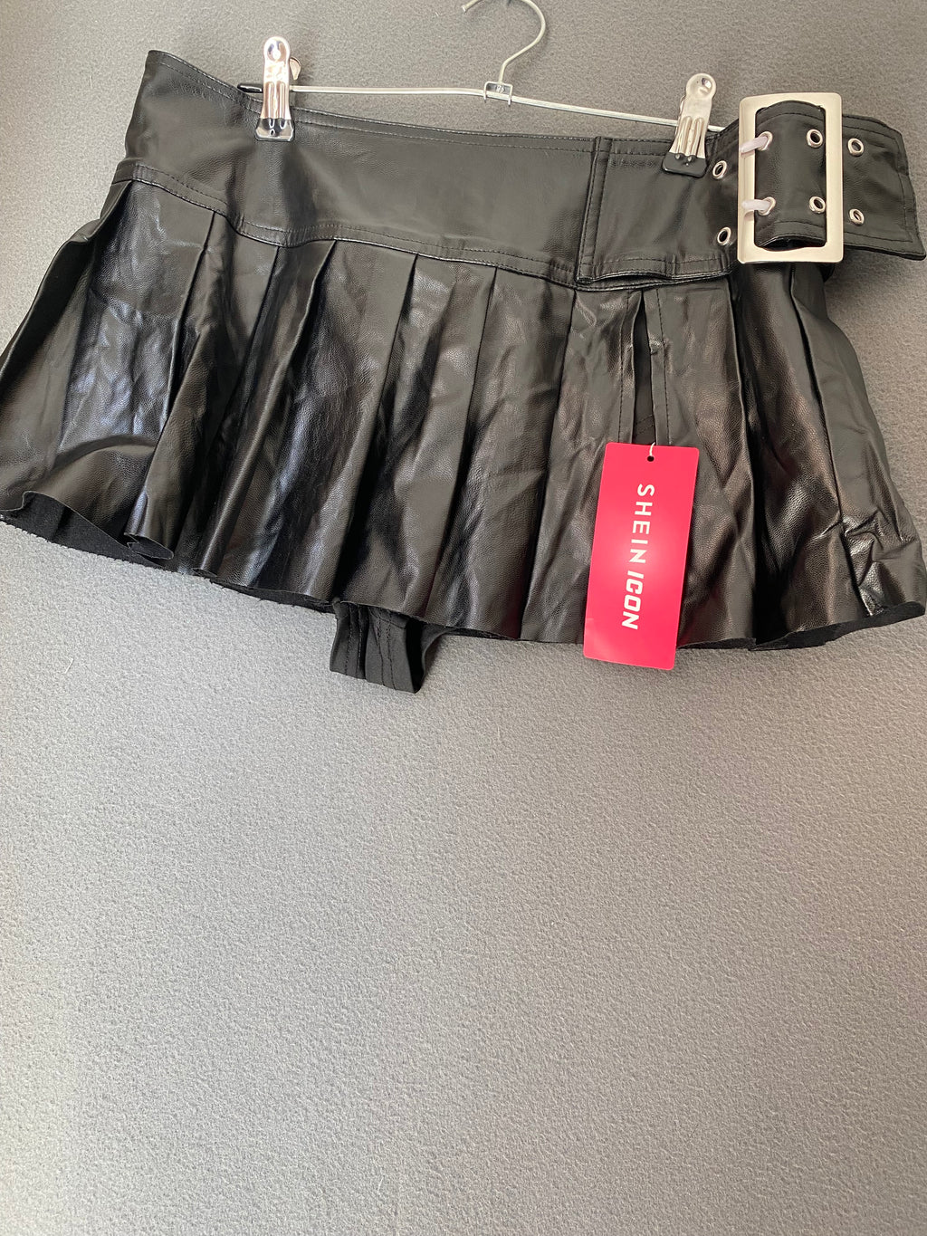 Mini-jupe plissée en simili cuir à grosse boucle